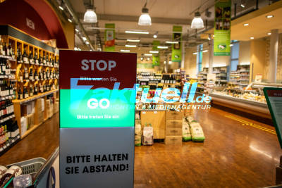 Einlass in Biomarkt per Ampel - Lichtschranke erfasst Kunden und regelt den Kundenverkehr - Chef desinfiziert persönlich Hände von Kunden