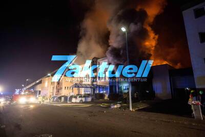 Großbrand zerstört Lagerhalle und umliegende Geschäftshäuser: Explosionen zu hören - Feuerwehr kämpft gegen meterhohe Flammen